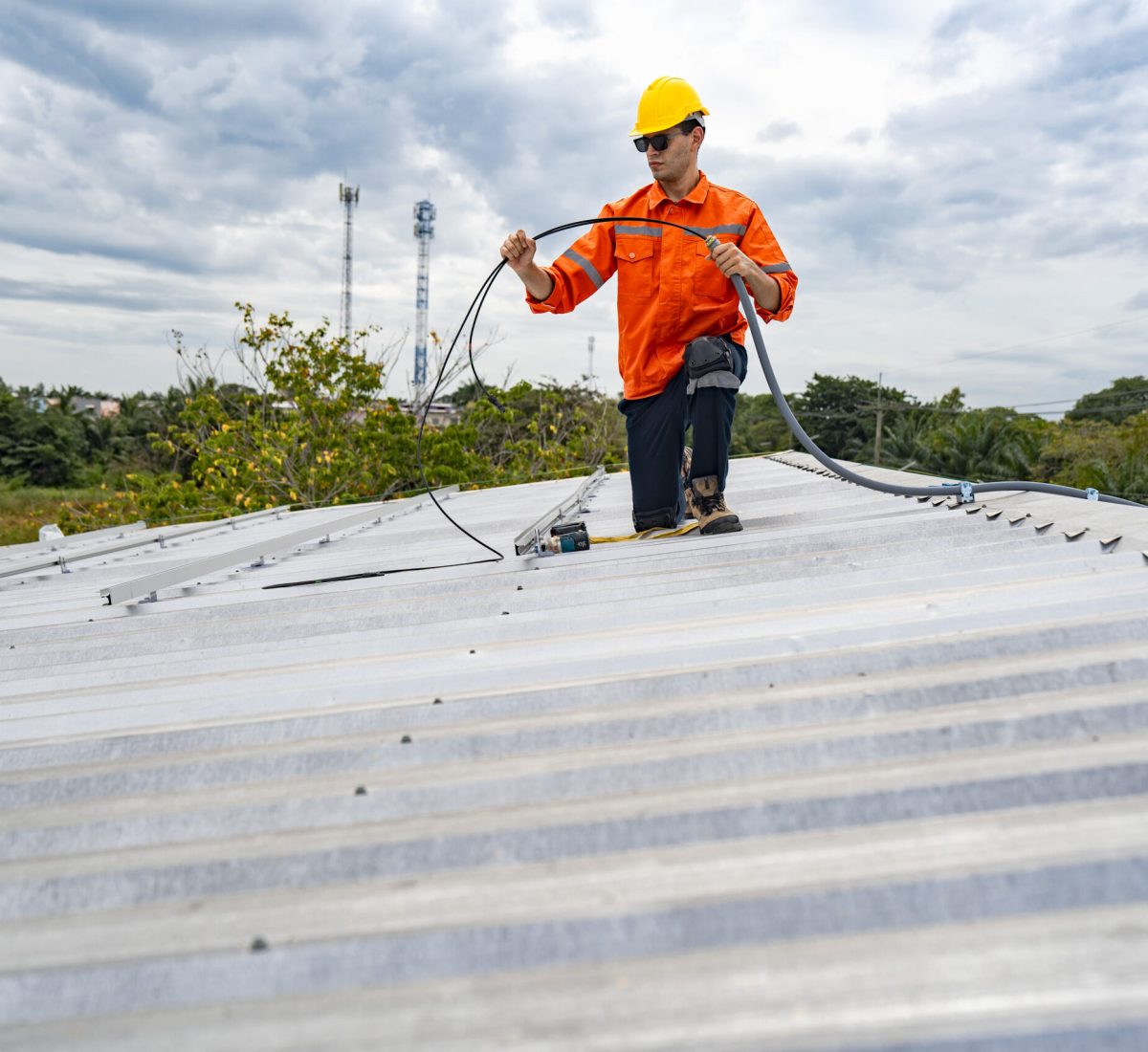 Technician in safety uniform and helmet kneeling on a rooftop, u Technician in safety uniform and helmet kneeling on a rooftop, using a drill for precise installation work. A scene highlighting safety, professionalism, and technical expertise in construction.