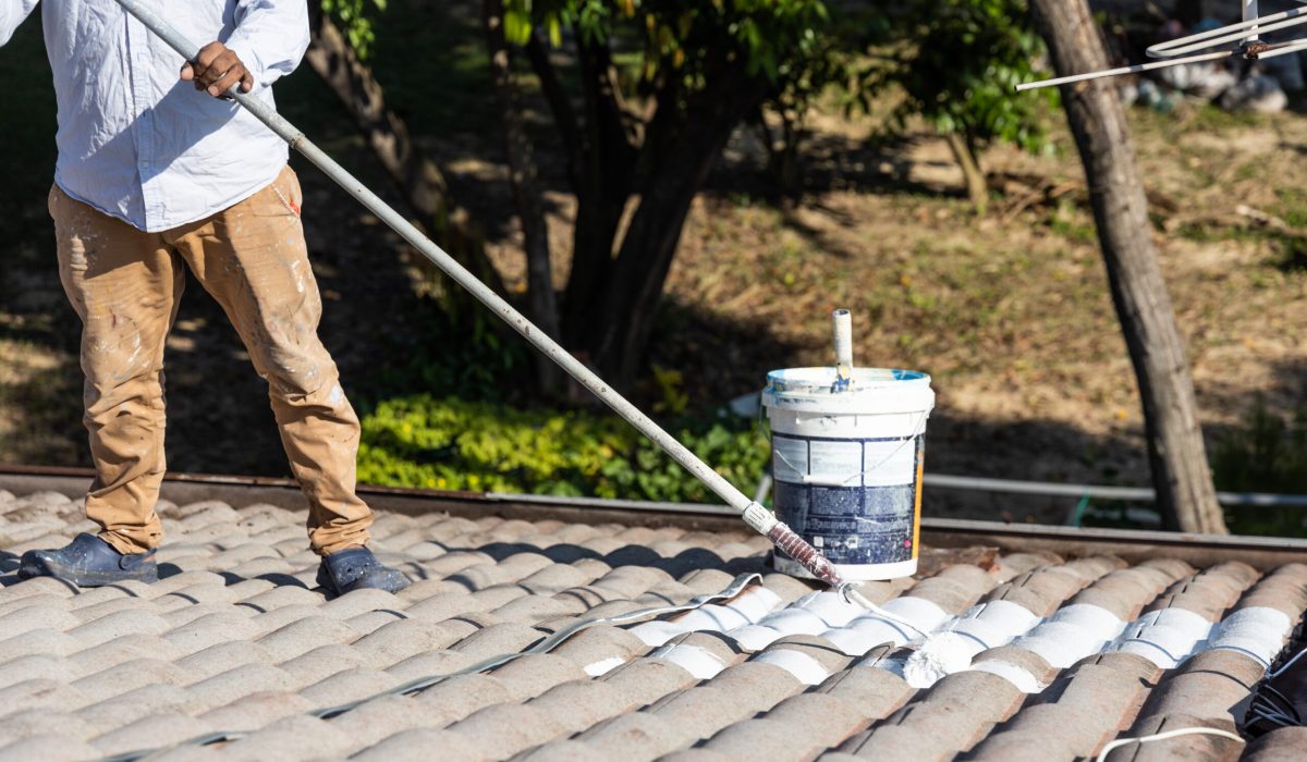 Worker adding undercoat foundation paint onto rooftop with roller at residential building in renovation Commercial Roof Coatings Services