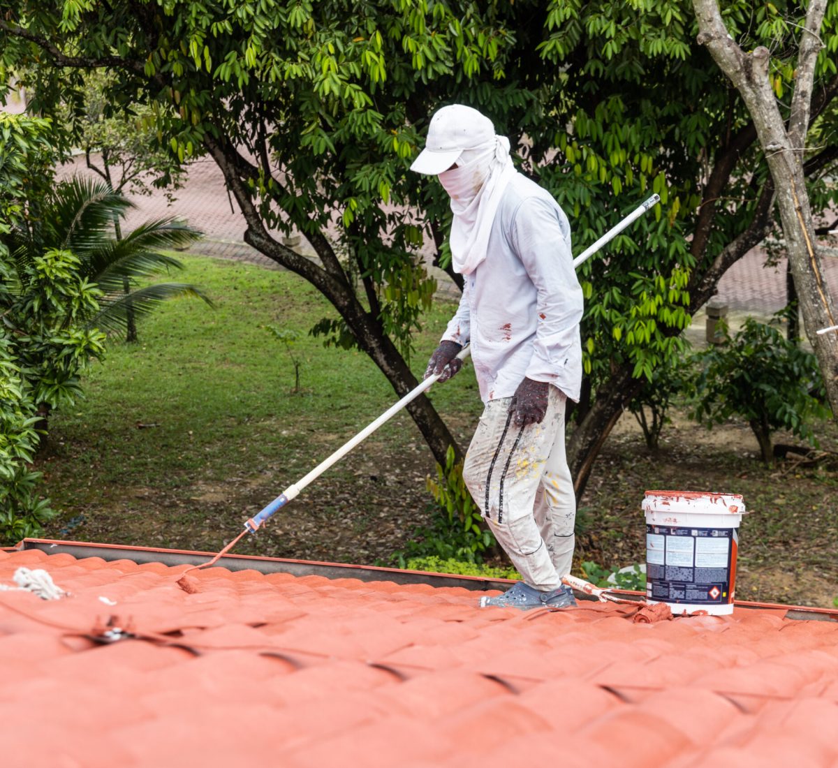 Worker painting red rooftop with roller at residential building during renovation Commercial Roof Coatings Services